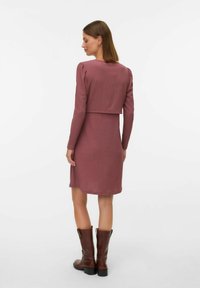Ribana obleka v barvi mauve do kolen, z dolgimi rokavi in kratkim zgornjim delom. Nosijo se z rjavimi, visokimi škornji s peto v kavbojskem slogu.