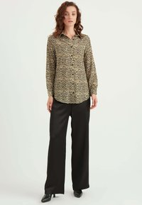 Bluse med leopardprint i let stof, med knaplukning fortil, lange ærmer og buet kant, parret med sorte vide bukser.