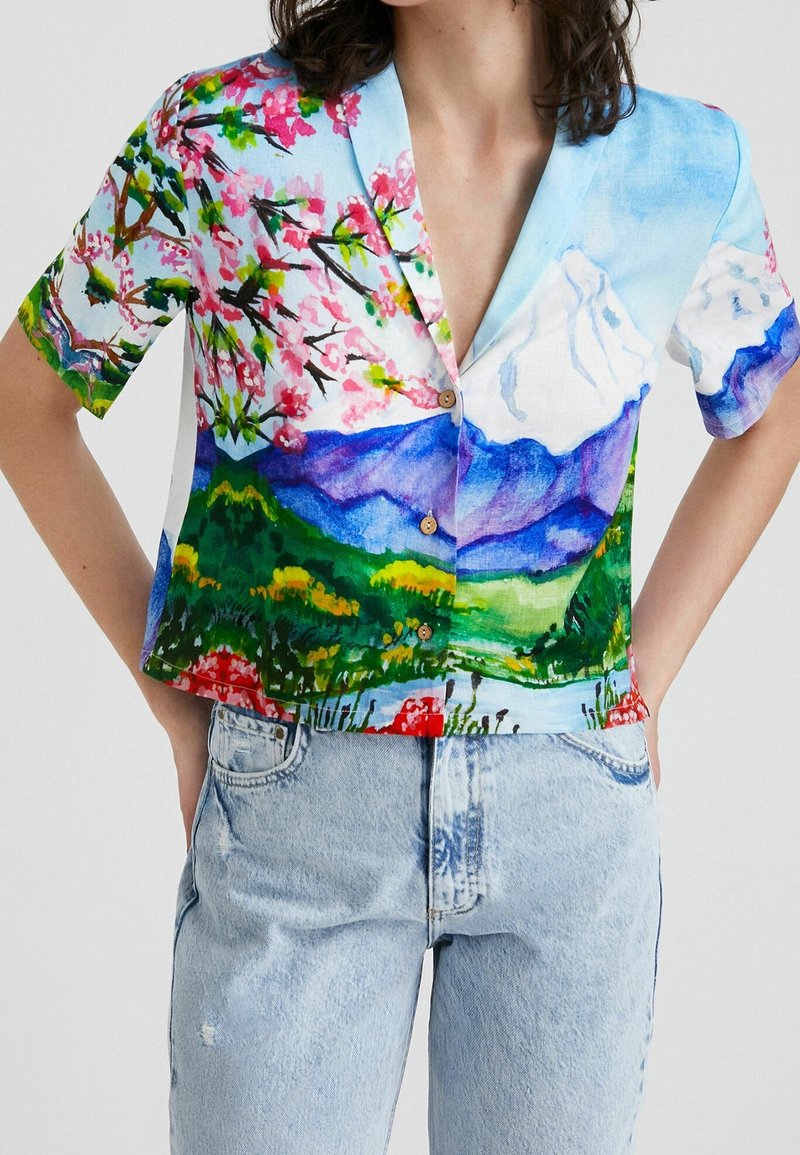 Chemise colorée à manches courtes avec imprimé floral et paysage, dotée d'un col pointu et de boutons en bois. Fabriquée en tissu léger.
