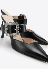 Sandali con tacco a stiletto in pelle nera con punta affusolata, fibbia decorata con strass e tacco a stiletto medio. Texture liscia.