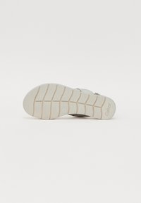 Light gray sandal sole with a textured surface, featuring horizontal ridges and a logo. The sole has subtle accents and a flexible design.