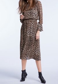 Midi-jurk met luipaardprint in bruin en zwart, met lange mouwen en een elastische taille. Draagt zwarte enkellaarzen. Lichtgewicht, doorschijnende stof.