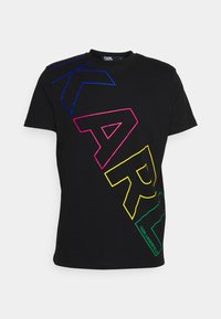 Černé tričko s krátkým rukávem se velkými barevnými obrysovými písmeny "KARL" diagonálně přes přední část a názvem značky "Karl Lagerfeld" v zelené barvě.