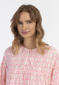 Ružovo-krémová tunika s kvetinovým vzorom, okrúhlym výstrihom, zapínaním na gombíky a zberaním. Ľahký materiál a voľný strih.