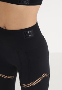 Černé sportovní legíny s vysokým pasem, texturovaným šitím a síťovinovými výřezy pro lepší prodyšnost, označené logem "IVY PARK".