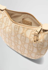 Sac à bandoulière beige en tissu texturé avec un motif de logo répété, une fermeture éclair et un accent en cuir lisse.