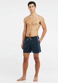 Marine zwembroek met een elastische tailleband en trekkoord, voorzien van zijzakken en een blauwe grafische print langs de linkerkant.