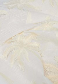 Tela blanca y suave con delicados bordados en relieve de patrones de palmeras que crean un diseño tropical sutil y texturizado.