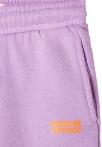 Lilac sweatpants made from textured fabric, featuring side pockets and orange "AMERICAN VINTAGE" logo embroidery near the hem.