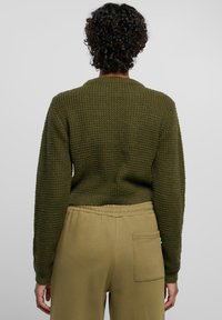 Oliven grønn strikket genser med et teksturert mønster, med ribbestrikket krage og mansjetter, båret med lyse beige, avslappede joggebukser.