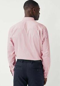 Helles rosa Langarmshirt mit klassischem Kragen, versehen mit einer Passe und geknöpften Manschetten, kombiniert mit dunkelblauen Hosen. Glatte Stofftextur.