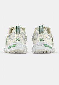 Bílé a zelené sportovní boty s texturovaným síťovinovým svrškem, označením GEL a polstrovanou podešví s jedinečným designem.