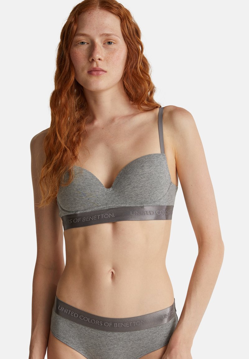 Šedá podprsenka a odpovídající pás s nápisem „UNIFIED COLORS OF BENETTON“. Měkký materiál s hladkou texturou a nastavitelné ramínka.
