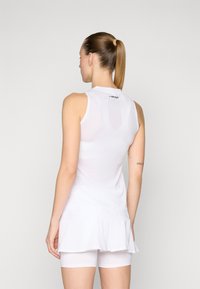 Top atlético branco sem mangas com um design de malha texturizada, apresentando um decote redondo e uma bainha com babados, usado com calções brancos.