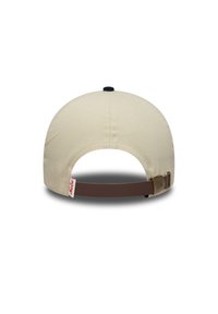 Μπεζ καπέλο με στρογγυλεμένο σχήμα, καφέ ρυθμιζόμενο λουράκι στο πίσω μέρος και ναυτικό κουμπί στην κορυφή. Διαθέτει ετικέτα με επωνυμία στο πλευρό.