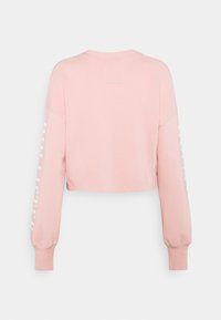 Kort roze sweatshirt met lange mouwen. Heeft witte tekst op één mouw en een ronde halslijn. Gemaakt van zacht, gestructureerd stof.