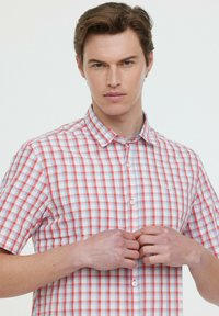 Chemise à manches courtes à carreaux rouge, bleu et blanc. Présente un design à boutons, un col pointu et un logo sur la poitrine.