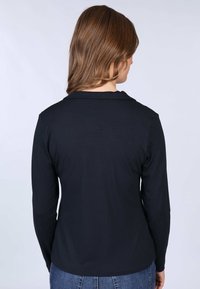 Black long-sleeve top made of soft fabric. Features a simple collar and rounded hem, paired with blue denim jeans.