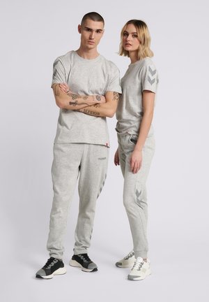 Modele męskie i damskie noszące pasujące jasnoszare bluzy i spodnie dresowe z akcentami w kształcie jodełki, stojące na jednolitym jasnym tle.