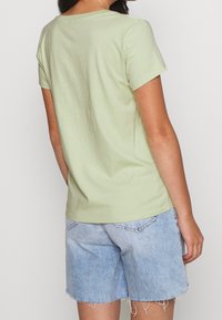 Jasnozielona bawełniana koszulka z krótkim rękawem i okrągłym dekoltem, połączona z jasnoniebieskimi szortami dżinsowymi z postrzępionymi brzegami.