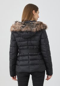 Jachetă puffer neagră cu o siluetă ajustată, având glugă căptușită cu blană faux, textură matlasată și o curea strânsă în talie.