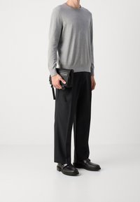 Harmaa neulepusero, musta vetoketjullinen olkalaukku, leveät mustat housut ja mustat kengät soljilla. Yksinkertainen muotoilu ja nykyaikainen tyyli.