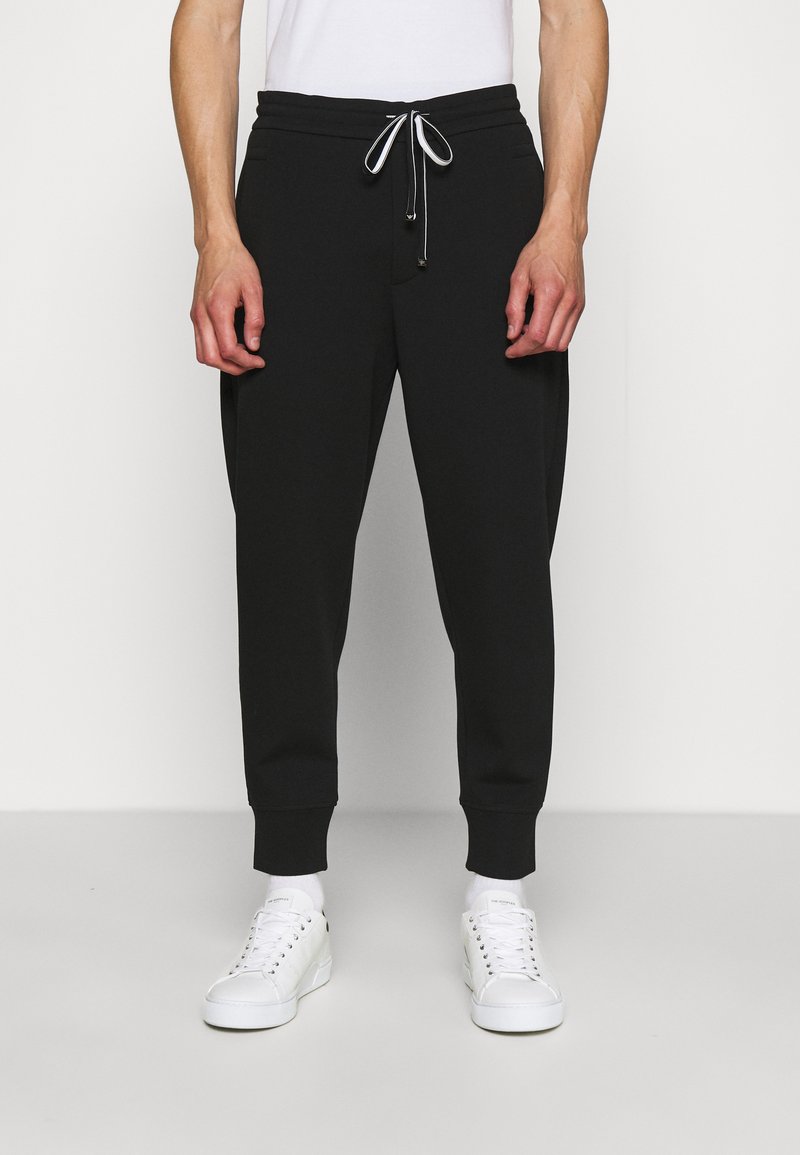 Zwarte joggingbroek met een trekkoord in de taille en elastische boorden, gemaakt van zachte stof. Geschikt bij witte sneakers en zichtbare enkelsokken.