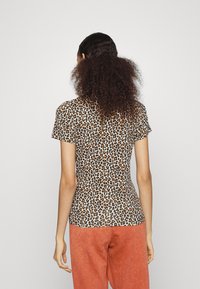 Korte mouwen, getailleerde top van een lichte, doorschijnende stof met een luipaardprint in bruin en zwart op een beige achtergrond.