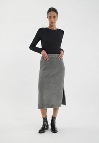 Haut à manches longues noir associé à une jupe midi en tricot grise avec une fente latérale et une ceinture à côtes. Complété par des bottines noires.