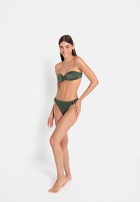 Πράσινο μπικίνι bandeau με συγκεντρωμένες λεπτομέρειες και δέσιμα στα πλάγια της κάτω πλευράς. Λείο υλικό, εφαρμοστή σχεδίαση, μινιμαλιστικό στυλ.