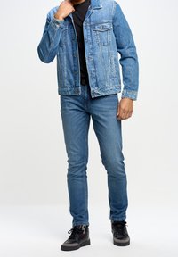 Jeansjacka med klassisk skärning, ljusblå färg, framfickor och knappstängningar, tillsammans med slim-fit blåjeans och svarta skor.