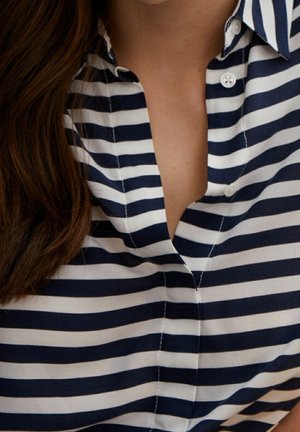 Chemise rayée bleu marine et blanche avec un col, présentant une fermeture à boutons à l'avant et un tissu texturé.