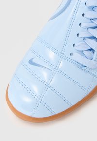 Sapato de pele azul claro, com acabamento brilhante e design acolchoado, fecho de atacadores e sola de borracha castanha. Apresenta um pequeno logótipo da Nike.
