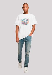 White t-shirt with a colorful soccer ball graphic, paired with distressed light blue jeans and white sneakers. Casual fit and style.