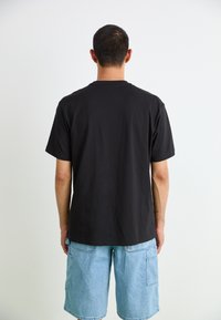 Black short-sleeved t-shirt made of cotton, with a relaxed fit, worn with light blue denim shorts featuring side pockets.