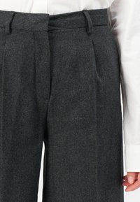 Pantalon en laine gris charbon à taille haute, avec une front plissé, des passants de ceinture et une coupe ajustée. Le tissu présente une texture lisse.