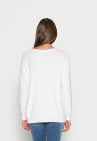 Maglione bianco oversize realizzato in un morbido tessuto testurizzato, con maniche lunghe e scollatura rotonda, abbinato a jeans azzurri chiari.