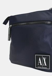 Pochette in nylon blu marina con cerniera nera e patch logotipo rettangolare bianco, con testo "AX" e "ARMANI EXCHANGE", finitura testurizzata.