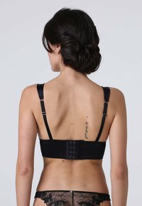 Reggiseno nero con spalline in satin regolabili, chiusura con gancetto e tessuto morbido. Presenta dettagli di cucitura e un motivo in pizzo decorativo sul fondo.