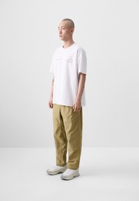 White t-shirt featuring a hexagonal graphic, paired with loose khaki pants and white sneakers. Simple design, casual fit, minimalistic style.