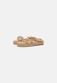 Beige braided sandals with woven straps and a thick textured sole. Flat design with a casual look. No visible hardware or embellishments.