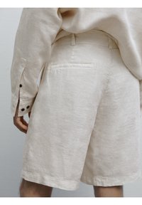 Lichtbeige linnen shorts met een gladde textuur, voorzien van een achterzak, riemlussen en een zoom die net boven de knie zit.