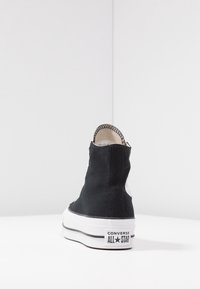 Czarne trampki za kostkę z płóciennym wierzchem i białą gumową podeszwą, z czarnym paskiem oraz logo Converse All Star na pięcie.