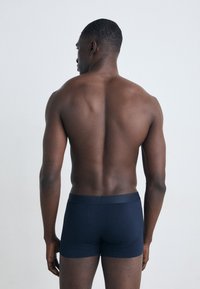 Sötétkék boxeralsó, amely puha, rugalmas anyagból készült, sima derékrésszel és testhez álló fazonnal, hátulról nézve.