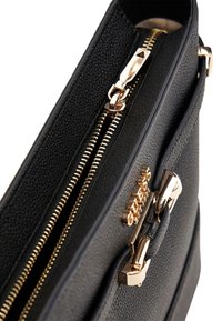 Bolso de mano texturizado en negro con herrajes dorados en la cremallera, que cuenta con dos compartimentos con cremallera y un detalle de logotipo metálico en la parte frontal.