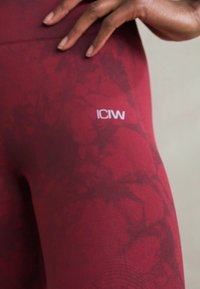 Bordové legíny s textúrovaným, mramorovým vzorom. Obsahujú biele logo "ICIW" blízko pásu. Hladký, elastický materiál.