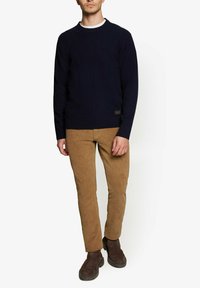 Marineblå striktrøje med rund hals, parret med lysebrune fløjlsbukser og brune ruskindsankelstøvler. Minimalistisk design, struktureret stof.