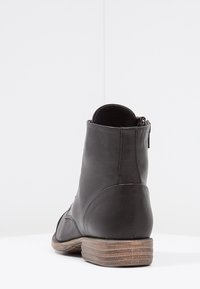 Stivaletto in pelle nera con finitura testurizzata, dotato di chiusura a zip e tacco in legno impilato. Design elegante e moderno con accenti minimal.