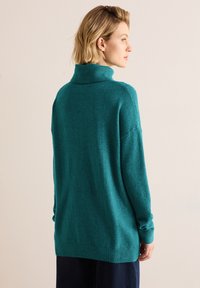Maglione a collo alto color teal realizzato in materiale morbido, con una vestibilità comoda, polsini a coste e orlo che si estende leggermente oltre la vita.