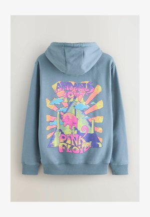 Mėlyna dėvima striukė su spalvingu grafikų dizainu, kuriame yra tekstas "Gyvūnai 1977" ir "Pink Floyd", vaizduojantys debesis, paršą ir abstrakčius formas.